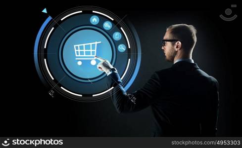 business, e-commerce, future technology, cyberspace and people - businessman in suit and glasses pointing finger to virtual shopping cart projection over black background. businessman pointing finger to shopping cart