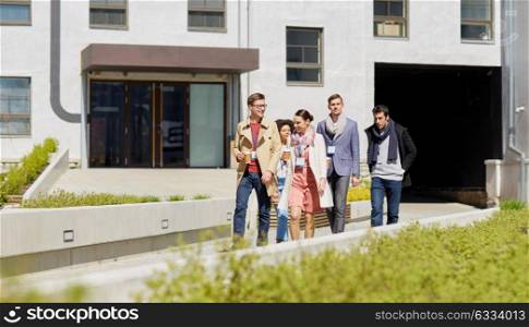 business, education and corporate concept - happy international group of office workers with conference badges drinking coffee and walking outdoors. office workers with coffee walking in city
