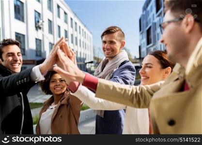 business, education and corporate concept - international group of people or students making high five on city street. group of happy people making high five in city