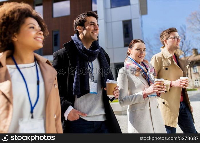 business, education and corporate concept - international group of people with coffee and conference badges on city street. people with coffee and conference badges in city