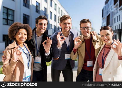 business, education and corporate concept - international group of people with conference badges showing ok hand sign on city street. business team with conference badges in city