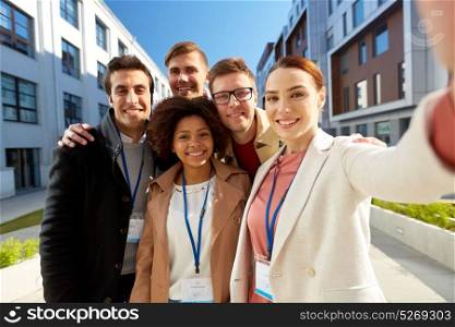 business, education and corporate concept - international group of people with conference badges taking selfie on city street. team with conference badges taking selfie in city