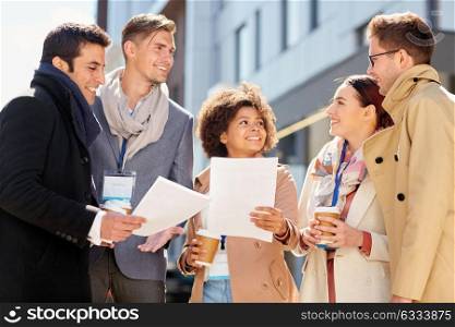 business, education and corporate concept - international group of people with papers, coffee and conference badges meeting outdoors. international business team with papers outdoors