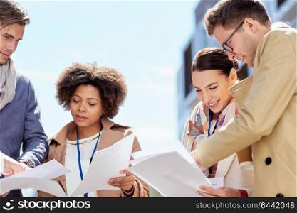 business, education and corporate concept - international group of people with papers and conference badges meeting outdoors. international business team with papers outdoors