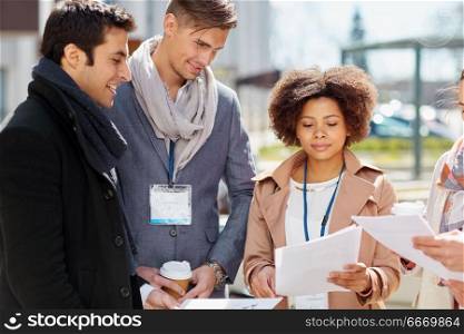 business, education and corporate concept - international group of people with papers and conference badges meeting outdoors. international business team with papers outdoors. international business team with papers outdoors