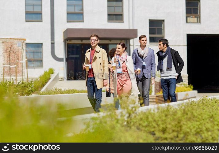 business, education and corporate people concept - happy international group of office workers with conference badges drinking coffee and talking outdoors. office workers with coffee on city street. office workers with coffee on city street