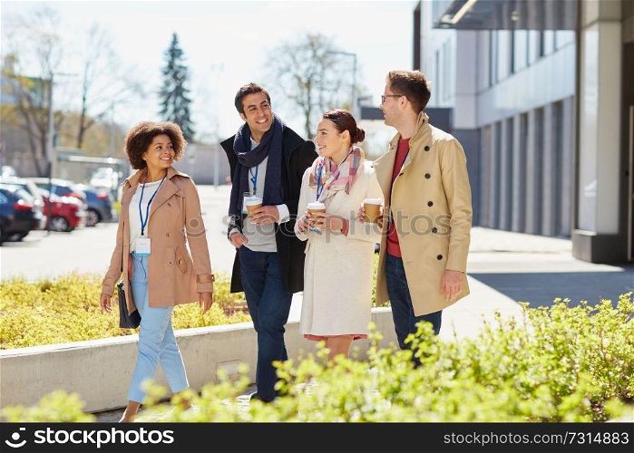 business, education and corporate people concept - happy international group of office workers with conference badges drinking coffee and talking outdoors. office workers with coffee on city street