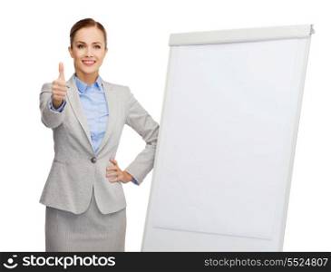 business, education and office concept - smiling businesswoman standing next to flip board and showing thumbs up