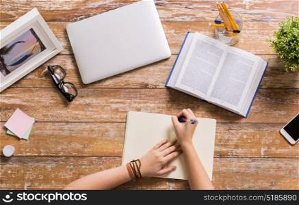 business, education and people concept - hands with book writing to notebook at wooden table. hands with book writing to notebook at table