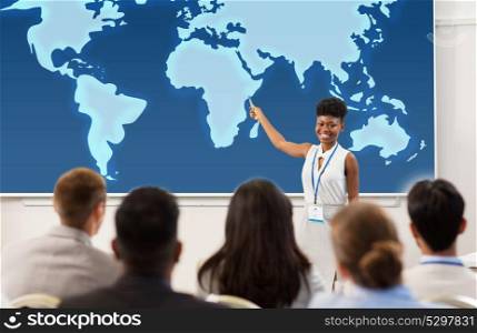 business, education and people concept - smiling african american businesswoman or lecturer showing world map on projection screen to group of students at conference presentation or lecture. group of people at business conference or lecture
