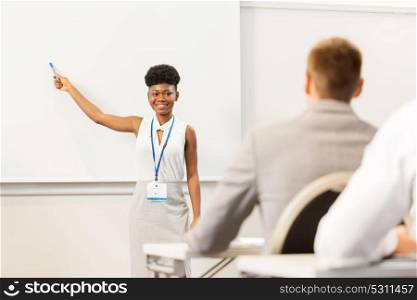 business, education and people concept - smiling african american businesswoman or lecturer with marker showing something on screen to group of students at conference presentation or lecture. group of people at business conference or lecture