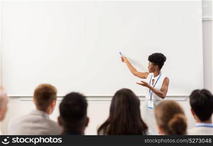 business, education and people concept - smiling african american businesswoman or teacher with marker showing something on screen to group of students at conference presentation or lecture. group of people at business conference or lecture