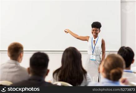 business, education and people concept - smiling african american businesswoman or teacher with remote and group of students at conference presentation or lecture. group of people at business conference or lecture