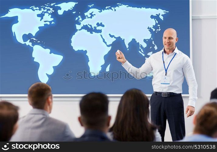 business, education and people concept - smiling businessman or lecturer with world map on projection screen and group of students at conference presentation or lecture. group of people at world business conference