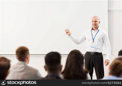 business, education and people concept - smiling businessman or teacher with remote and group of students at conference presentation or lecture. group of people at business conference or lecture