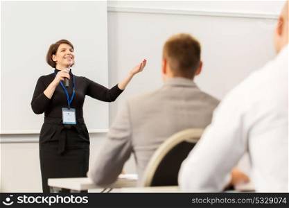 business, education and people concept - smiling businesswoman or lecturer with microphone talking to group of students at conference presentation or lecture. group of people at business conference or lecture