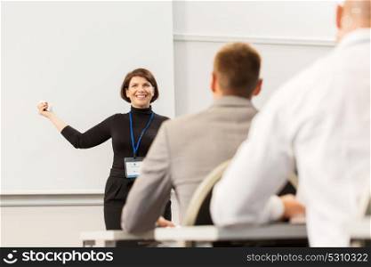 business, education and people concept - smiling businesswoman or lecturer with remote and group of students at conference presentation or lecture. group of people at business conference or lecture