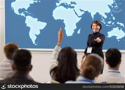 business, education and people concept - smiling businesswoman or lecturer with world map on projection screen answering questions at conference presentation or lecture. group of people at business conference or lecture