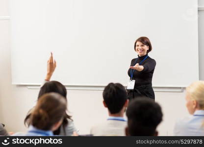 business, education and people concept - smiling businesswoman or teacher answering questions at conference presentation or lecture. group of people at business conference or lecture