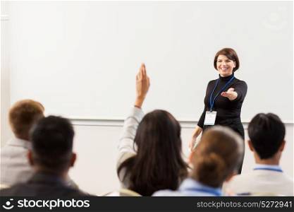 business, education and people concept - smiling businesswoman or teacher with remote answering questions at conference presentation or lecture. group of people at business conference or lecture