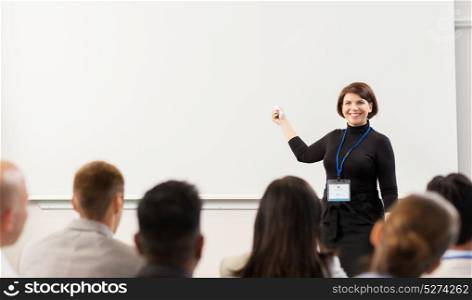 business, education and people concept - smiling businesswoman or teacher with remote and group of students at conference presentation or lecture. group of people at business conference or lecture