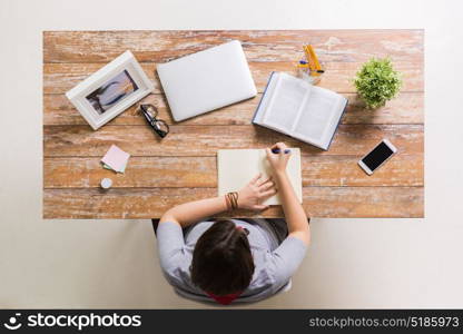 business, education and people concept - woman with book writing to notebook at wooden table. woman with book writing to notebook at table