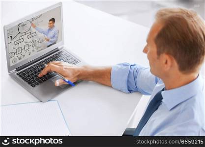 business, education and technology concept - businessman watching webinar on laptop computer at office. businessman watching webinar on laptop at office