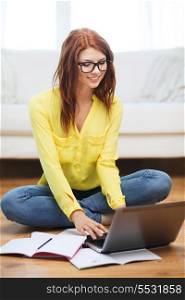 business, education and technology concept - smiling female student in eyeglasses with notebooks and laptop computer at home