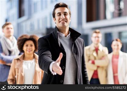 business, education, gesture and corporate concept - group of happy people and man giving hand for handshake on city street. man giving hand for handshake on city street