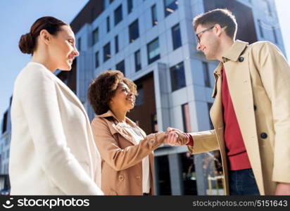 business, education, gesture and corporate concept - happy people shaking hands on city street. happy people shaking hands on city street