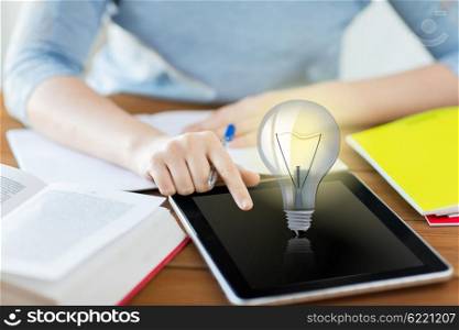 business, education, idea, technology and people concept - close up of student woman with light bulb on tablet pc computer and notebook at home