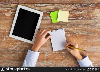 business, education, people and technology concept - close up of female hands with tablet pc computer and stickers writing to notebook on wooden table. close up of hands with tablet pc and notebook