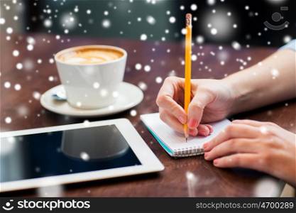 business, education, people and technology concept - woman hands writing to notebook by pencil and tablet pc computer with coffee over snow