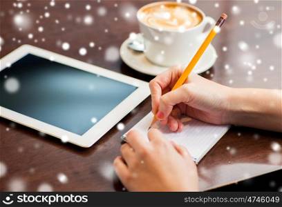 business, education, people and technology concept - woman hands writing to notebook by pencil and tablet pc computer with coffee over snow