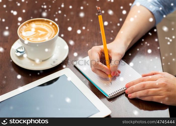 business, education, people, technology and lifestyle concept - close up of woman hands writing to notebook by pencil and tablet pc computer with coffee over snow