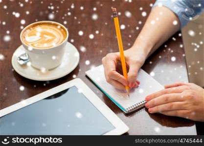 business, education, people, technology and lifestyle concept - close up of woman hands writing to notebook by pencil and tablet pc computer with coffee over snow