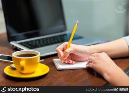 business, education, people, technology and lifestyle concept - close up of woman writing to notebook with pencil