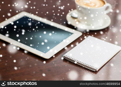 business, education, technology and object concept - close up of notebook with tablet pc computer and coffee on table over snow