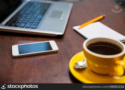 business, education, technology and object concept - close up of smartphone, coffee cup and laptop on table