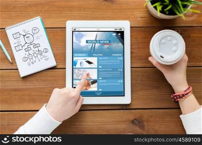 business, education, technology and people concept - close up of woman with internet news application on tablet pc computer screen, notebook and coffee on wooden table