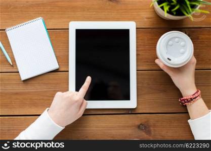 business, education, technology and people concept - close up of woman with blank tablet pc computer screen, notebook and coffee on wooden table