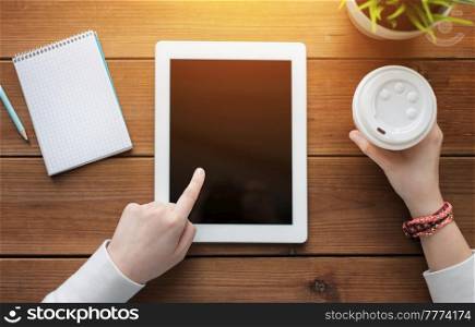 business, education, technology and people concept - close up of woman with blank tablet pc computer screen, notebook and coffee on wooden table. close up of woman with tablet pc on wooden table