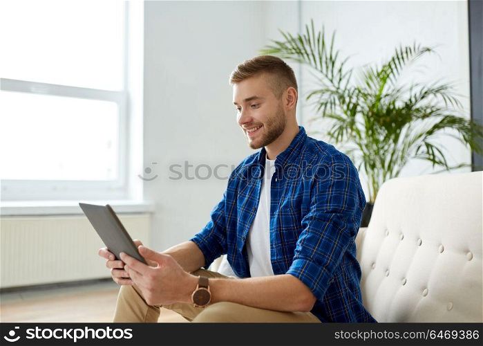 business, education, technology and people concept - happy smiling man with tablet pc sitting on sofa at office. happy smiling man with tablet pc at office