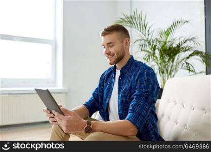 business, education, technology and people concept - happy smiling man with tablet pc sitting on sofa at office. happy smiling man with tablet pc at office