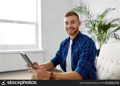 business, education, technology and people concept - happy smiling man with tablet pc sitting on sofa at office. happy smiling man with tablet pc at office. happy smiling man with tablet pc at office
