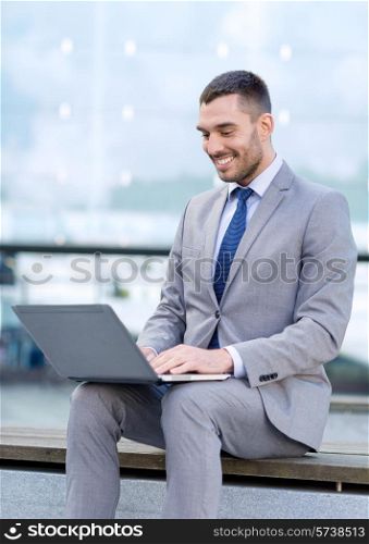 business, education, technology and people concept - smiling businessman working with laptop computer on city street