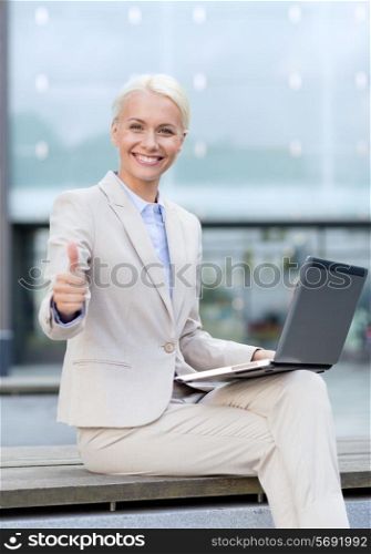 business, education, technology and people concept - smiling businesswoman working with laptop computer on city street