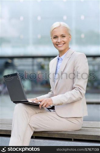 business, education, technology and people concept - smiling businesswoman working with laptop computer on city street
