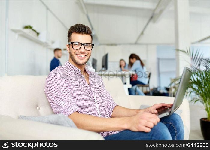 business, education, technology and people concept - smiling young man in eyeglasses with laptop computer working at office. man in eyeglasses with laptop working at office