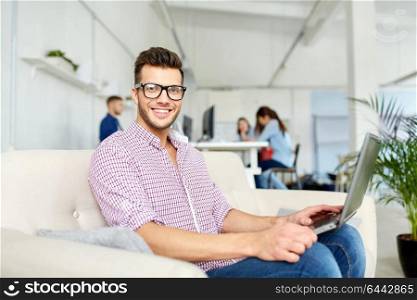 business, education, technology and people concept - smiling young man in eyeglasses with laptop computer working at office. man in eyeglasses with laptop working at office
